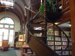 Spiral staircase with plant at top in foreground and shelves of books in background