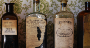 Four Apothecary Bottles against a white/green floral old time wallpaper