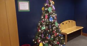 6 foot christmas tree decorated with lights, ornaments, and paper ornaments standing next to a wooden bench