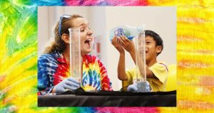 Picture of Woman laughing with boy putting dish soap into a graduated cylinder on a Tie Dye background