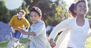 Two smiling children outside being chased by an older teen female