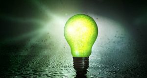 Green glowing lightbulb on dark wet surface