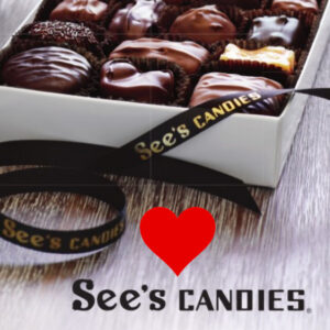 A chocolate and caramel candy on a plate on the left with a box of various chocolate candies to its right and below both a red heart and the words See's Candies