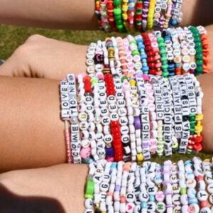 Four light skinned arms full of Taylor Swift style bracelets with sayings on them