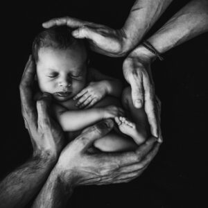 Black and white photo with four hands holding an infant in them