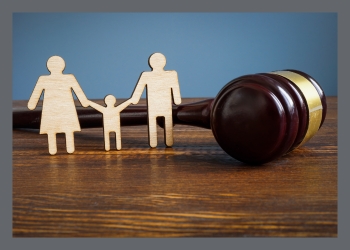 Three wooden cutout people, two adults and a child leaned up against a gavel on a wooden desk