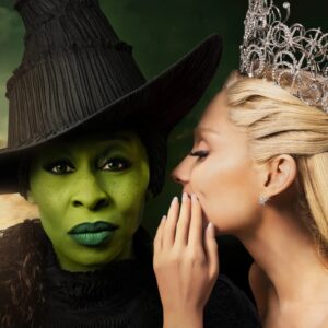 A light skinned woman wearing a tiara whispering behind her hand to a green skinned woman with green lips wearing a witches hat